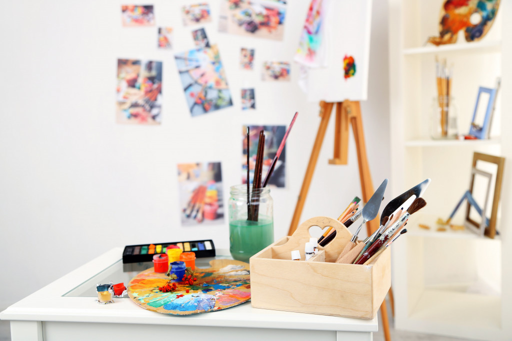 art supplies and paint in the table with artworks in the background